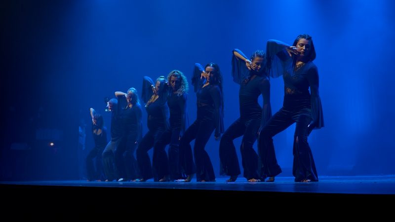 Le groupe en noir sur une scène bleue, une main posée sur la tête.