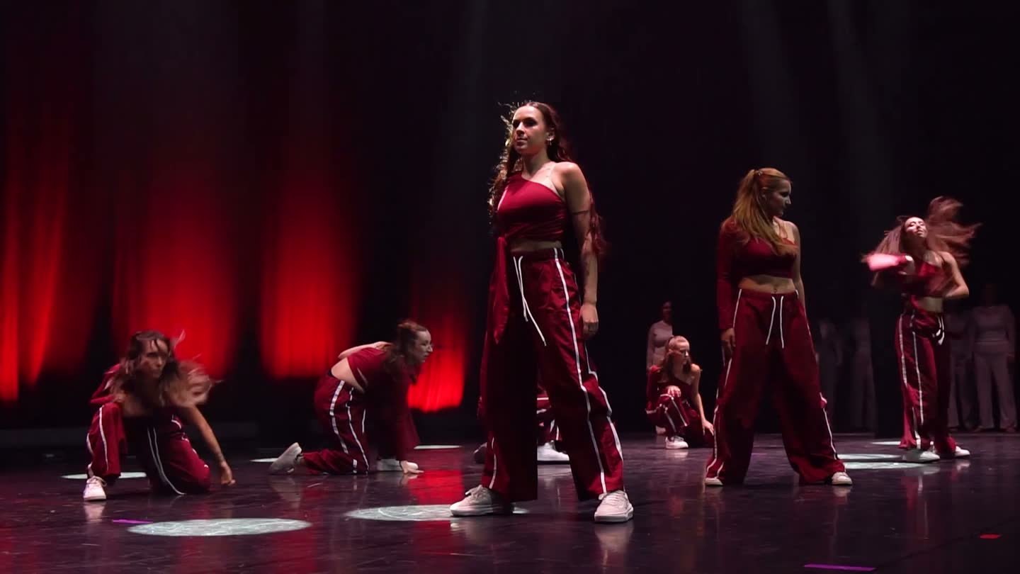 Le groupe hip-hop niveau 2 sur scène, en survêtements bordeaux, sous une lumière rouge.
