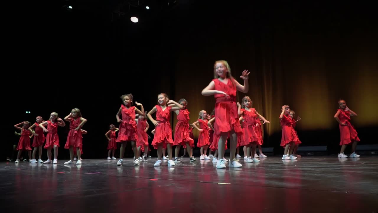 Les danseuses du groupe Girly en robes rouges, bras levés, dans une lumière chaude.