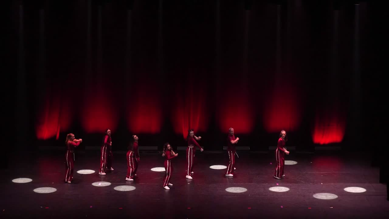 Le groupe hip-hop niveau 2 en survêtements bordeaux à bandes blanches, en pleine action sous une lumière rouge.