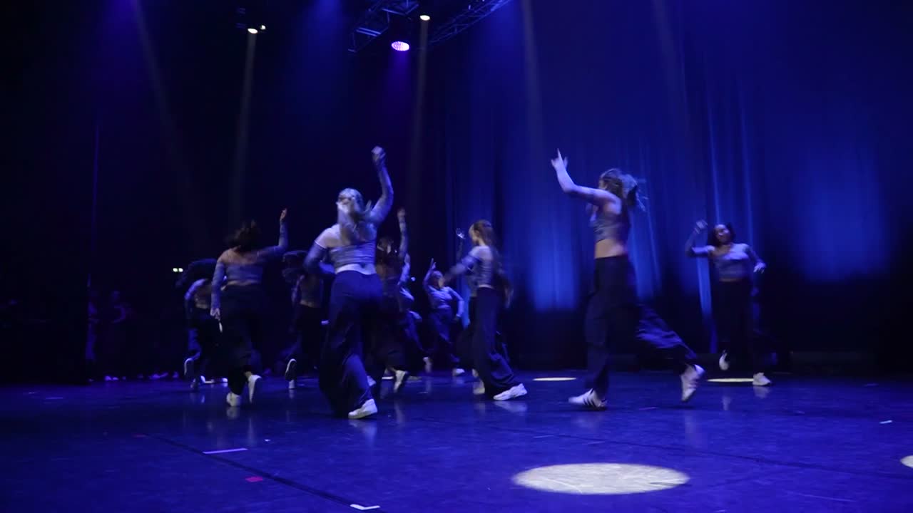 Le groupe lady niveau 1 en noir, sur une scène bleu profond ponctuée de ronds de lumière.